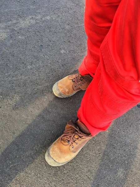 The lower of the feet of a healthy safety and environmental officer who wears a red uniform (pants) and brown safety shoes.
