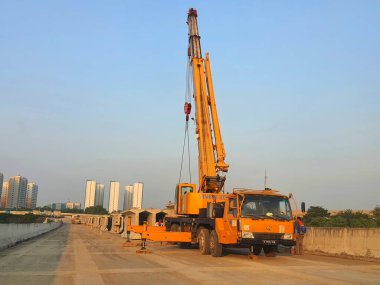 A yellow crane is lifting the segmental precast girder. This is the process of arranging the girder segments in position before joining the segments with the steel strand.