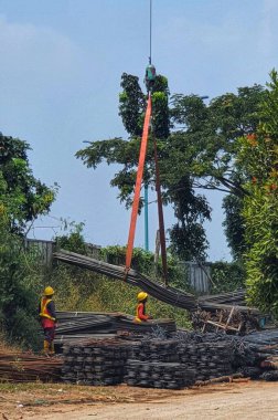 Two construction workers are mobilizing pieces of structural steel. This process is carried out with the help of cranes and slings, the workers just hang the sling to the steel material and then the steel material is moved by crane, and is accepted b