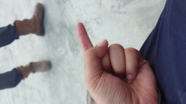 Vertically frame video of a girl's hand that counting from one to five in construction site, while a person in safety shoes walking in the background with a blur condition.
