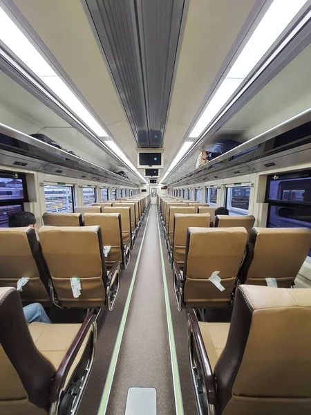 Premium economy train passenger seats in Indonesia. With a calm and soothing brown color. There are four seats in a row, two seats on the right and two on the left and there is space to walk in the middle.