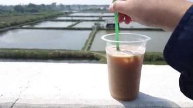 Someone is stirring iced coffee in a plastic cup using a green straw.