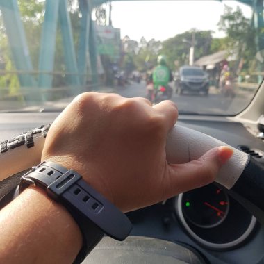 A hand is holding the steering wheel. The hand is wearing a black rubber band.