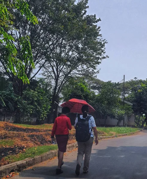 Jakarta in August 2022. A mother is picking up her child from school, because the weather is very hot they use red umbrellas to protect them from the hot sun.