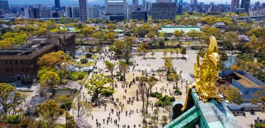 Osaka Şatosu 'nun güney manzarası, Osaka City' deki Osaka gökdelenlerinin manzarası ve arka planda turistlerle dolu olan Kale 'nin etrafındaki parkın manzarası ile altın balıkların dekore ettiği çatıdan görülüyor..