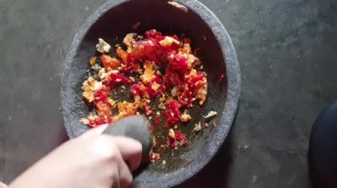 Biber sosu yapma süreci. Bir el, kırmızı biber sosu yapmak için soğan ve biberi taş bir havan topağında eziyor..