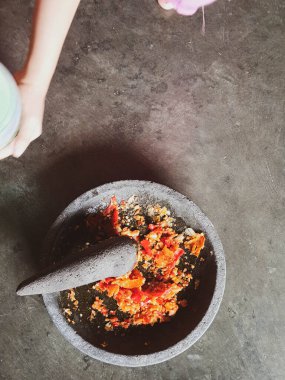 Biber sosu yapma süreci. Bir el, kırmızı biber sosu yapmak için soğan ve biberi taş bir havan topağında eziyor..