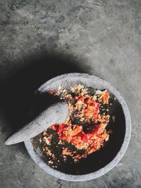 Biber sosu yapma süreci. Bir el, kırmızı biber sosu yapmak için soğan ve biberi taş bir havan topağında eziyor..