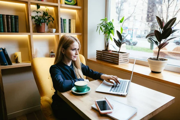 Girl working at a computer near the window with a cup of coffee