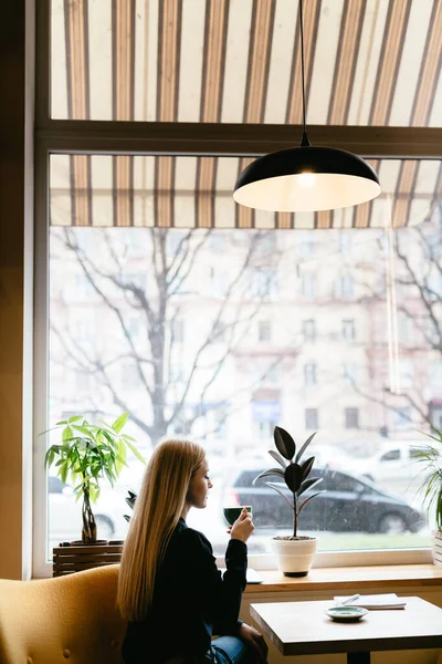 Girl sitting in a cafe near the window with a cup of coffee