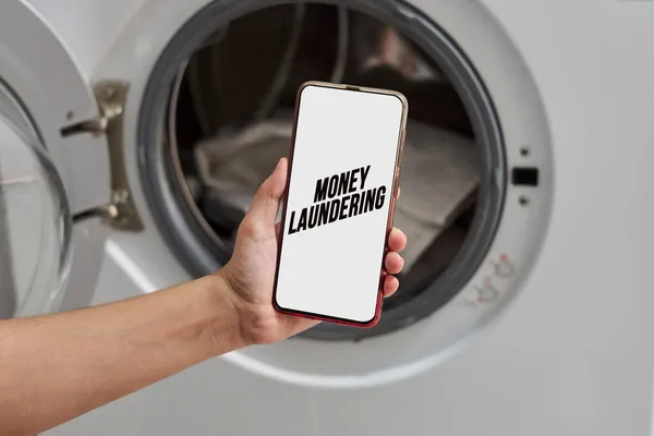 Money laundering concept - A person holding smartphone over washing machine