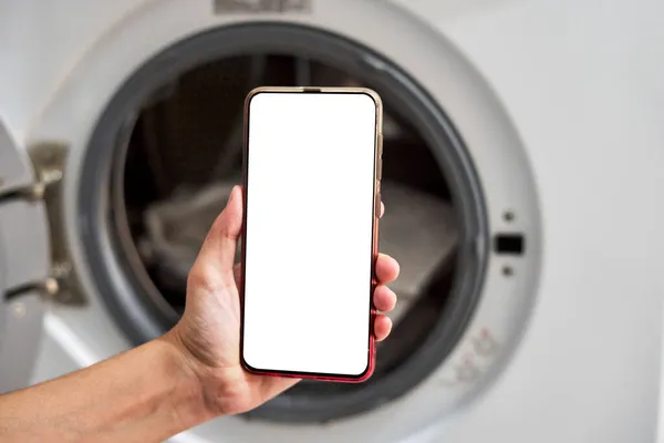 Seseorang memegang smartphone dengan layar kosong di dekat mesin cuci — Stok Foto
