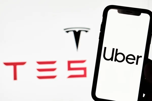 Una persona tiene un teléfono inteligente con marca registrada Uber con el logotipo de Tesla — Foto de Stock