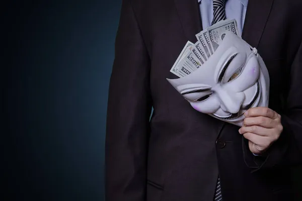一个穿着正式衣服的神秘莫测的人拿着匿名面具和堆积如山的美元 — 图库照片