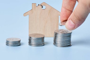 Erkek eli bozuk para yığınına para koyarken mavi arka planda ahşap ev vardı. Ev almak için para biriktiriyorum, ev kredisi için finansal plan yapıyorum. Kapat..