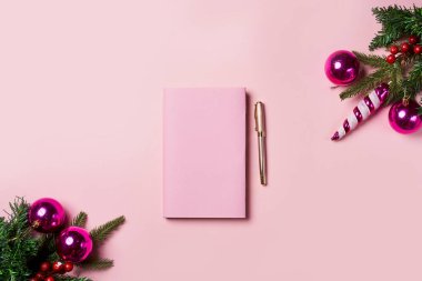 Kalemli pembe defter ve beyaz arka planda pembe toplarla süslenmiş Noel ağacı dalları. Zarif Noel kadınsı çalışma alanı üst görünümü.