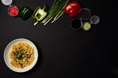 Anında erişte kompozisyonu. Erişteler, taze sebzeler ve baharatlar parlak siyah arka planda.