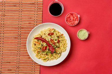 Anında erişte kompozisyonu. Şehriyeler, taze sebzeler ve baharatlar parlak kırmızı arka planda.