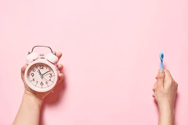 朝のコンセプト ピンクの目覚まし時計とピンクの背景に若い女性の手の歯ブラシ — ストック写真