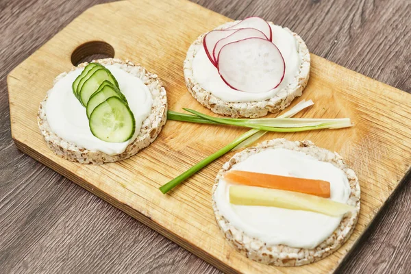 Rice cake with cream cheese and vegetables on wooden board