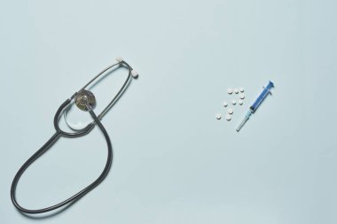 Tek kullanımlık şırınga, stetoskopen ve mavi arka planda beyaz yuvarlak tabletler..