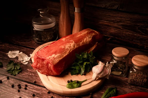 Meat on a wooden table with addition of fresh herbs and aromatic spices. Natural product from organic farm, produced by traditional methods