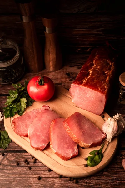 Sliced smoked meat on a wooden table with addition of fresh herbs and aromatic spices. Natural product from organic farm, produced by traditional methods