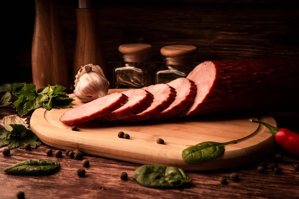 Sliced smoked meat on a wooden table with addition of fresh herbs and aromatic spices. Natural product from organic farm, produced by traditional methods