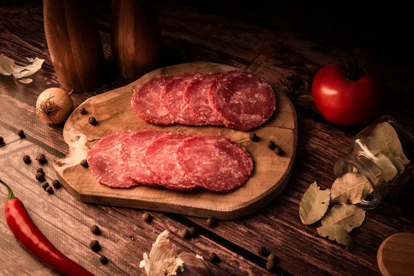 Sliced smoked meat on a wooden table with addition of fresh herbs and aromatic spices. Natural product from organic farm, produced by traditional methods