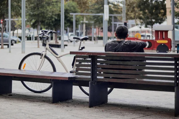 An unrecognizable Caucasian single person in selective focus sitting on her back on a park bench next to her bicycle relaxing