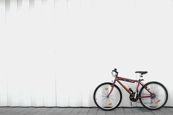 Single red mountain bike without people located on the lower right side of the image and leaning against a white wall with some black stripes and with space for text on top