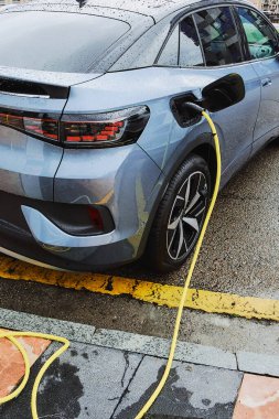 Yağmurlu bir günde elektrik kablosuna bağlı elektrikli bir araba. Fosil yakıtları CO2 yayan geleneksel araçlarda bir enerji kaynağı olarak değiştirme kavramı.