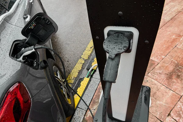 Electric car on a rainy day connected to its charging cable. Concept of replacing fossil fuels as a source of energy in traditional vehicles that emit CO2.