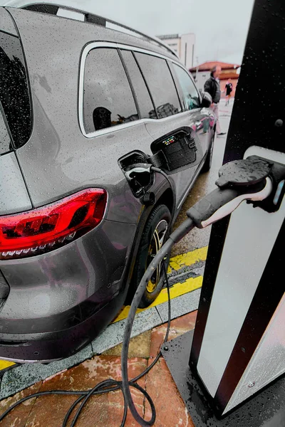 Electric car on a rainy day connected to its charging cable. Concept of replacing fossil fuels as a source of energy in traditional vehicles that emit CO2.