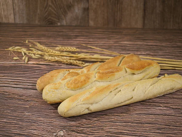 Homemade french style loaves of bread on wooden background and with wheat and oatmeal decoration.