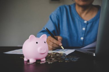 a woman makes calculations, checks her finances, makes notes in a notebook and sets aside some of the funds, savings in a piggy bank