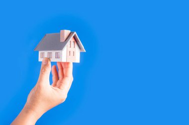 Female hands holding small model house on blue background