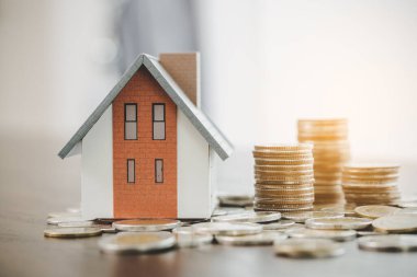 House model and money coins stacks on blur table background. Savings plans for home, loan, investment, mortgage, finance and banking about house concept.