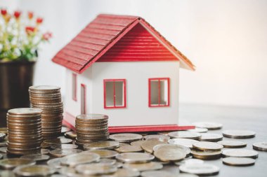 House model and money coins stacks on blur table background. Savings plans for home, loan, investment, mortgage, finance and banking about house concept.