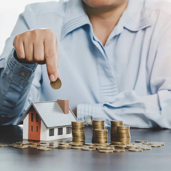 Hand putting coin in house model of coin for saving money for buying house. Savings plans for home, loan, investment, mortgage, finance and banking about house concept.