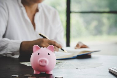 a woman makes calculations, checks her finances, makes notes in a notebook and sets aside some of the funds, savings in a piggy bank