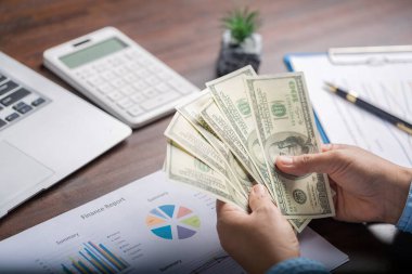Close up young business woman using counting cash money one hundred dollar bills, checking financial documents, sitting at table with papers and tax form, managing planning budget, accounting expenses