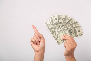 Close up woman holding dollars happy pointing with hand and finger to the side successful, showing money and boasting lottery winning, big profit. indoor studio shot isolated on gray background