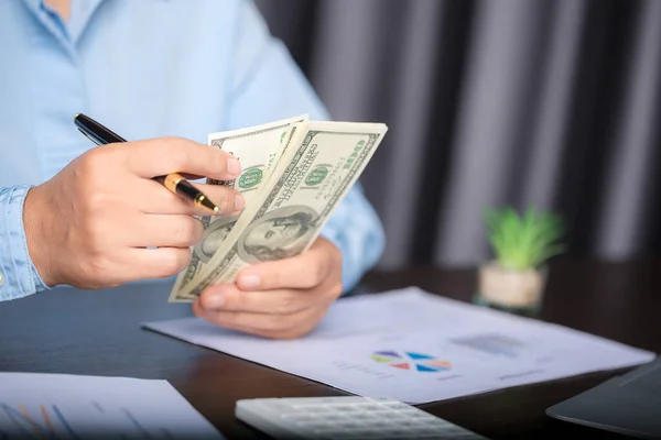 Close up young business woman using counting cash money one hundred dollar bills, checking financial documents, sitting at table with papers and tax form, managing planning budget, accounting expenses