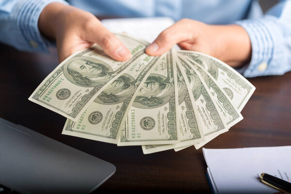 Закрыть молодую деловую женщину, используя подсчет наличных денег стодолларовые купюры, проверку финансовых документов, сидение за столом с бумагами и налоговой формой, управление бюджетом планирования, бухгалтерские расходы