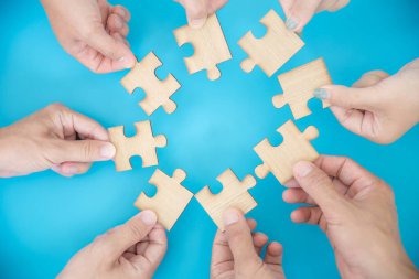 High Angle View Of Businesspeople Hand Solving Jigsaw Puzzle On Blue Background