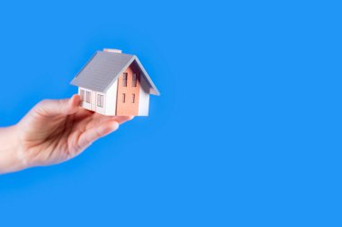 Female hands holding small model house on blue background