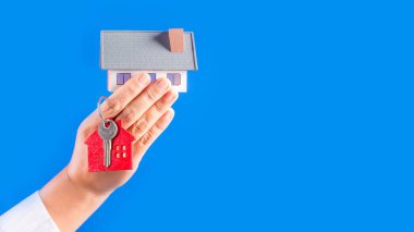 Female hands holding little model house with key  on blue background