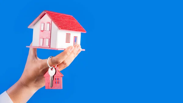 Female hands holding little model house with key  on blue background