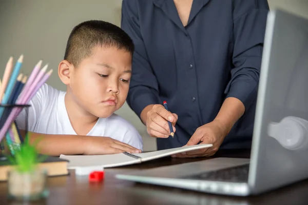 Young student distance learning virtual distance online class on video call virtual lesson with mother, studying at home using laptop computer. Parent or tutor teaching child boy with remote education